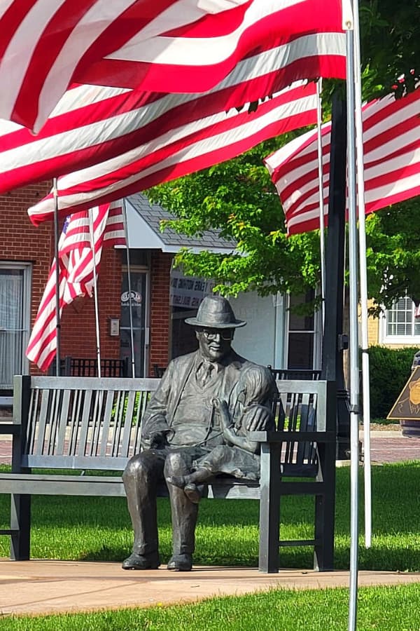 American flag by a statue of old man and child in a park